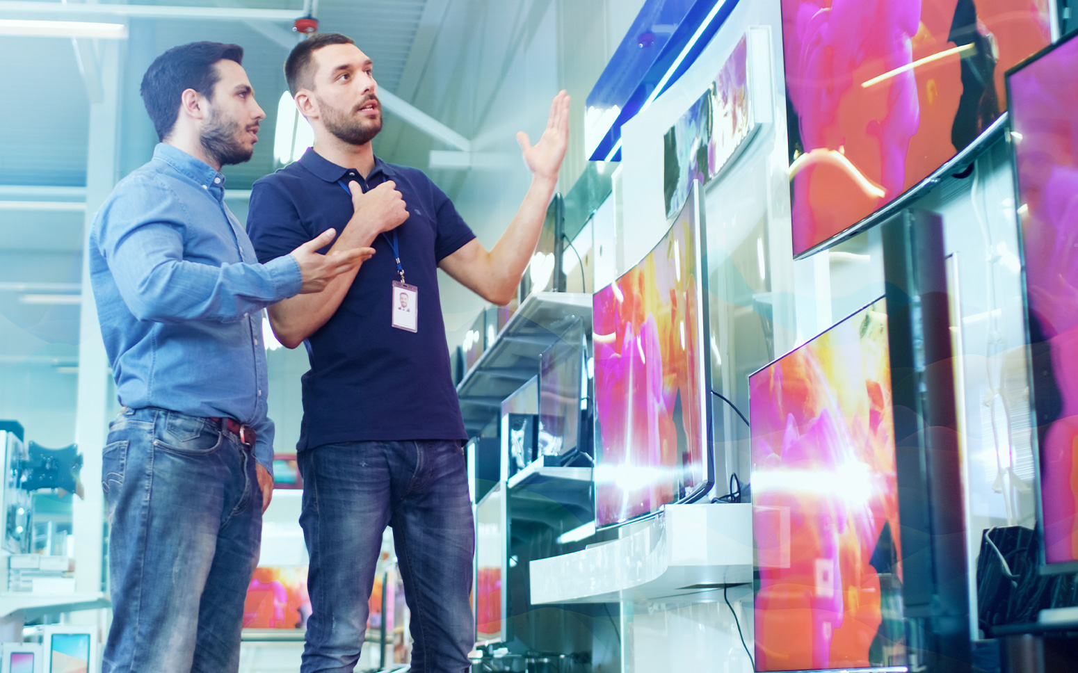 Two gentlemen discuss consumer electronics sales in front of a giant tv. 