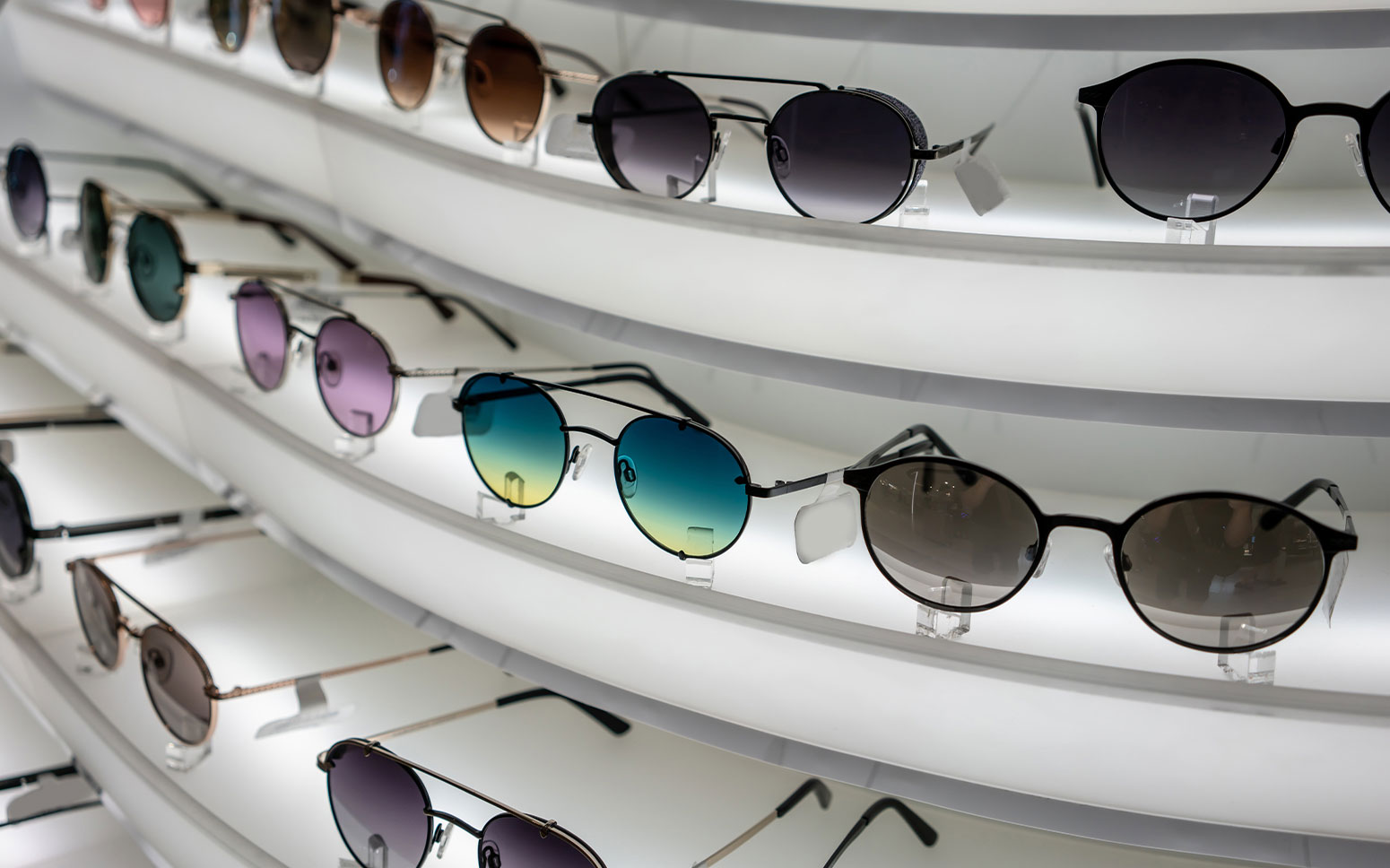 Luxury retail sunglasses adorn white, curved shelves. 
